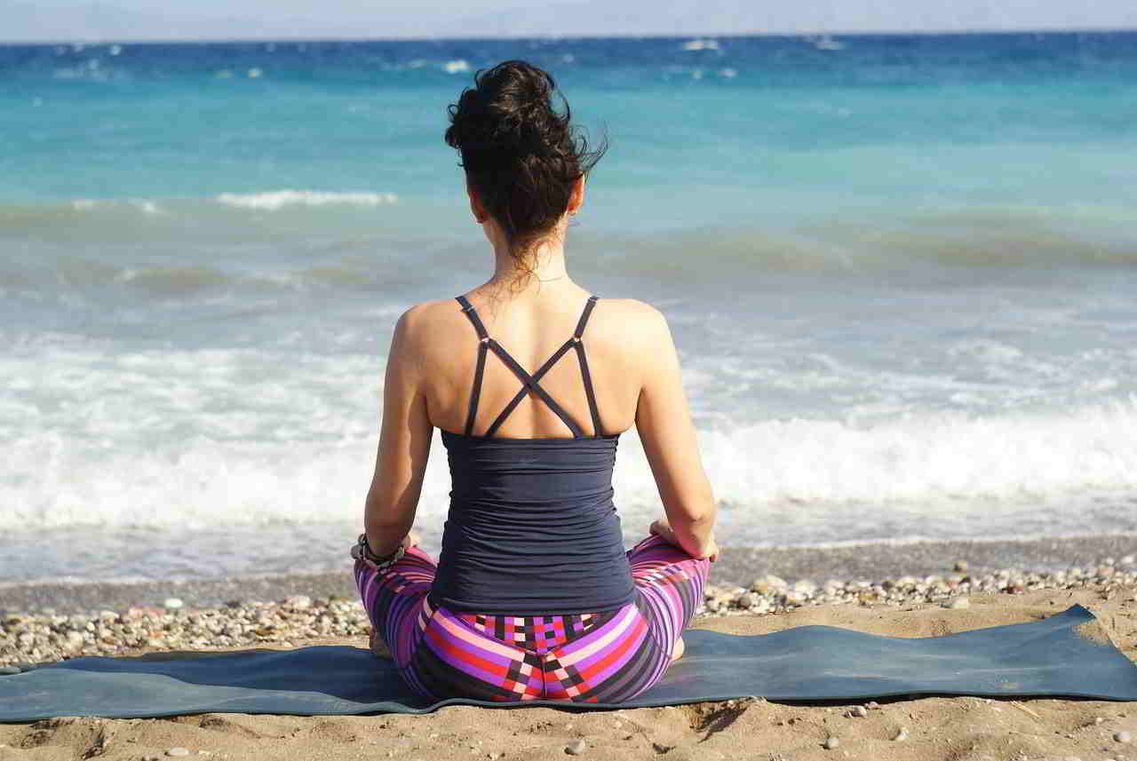 Woman facing the ocean meditating and sitting on the sand